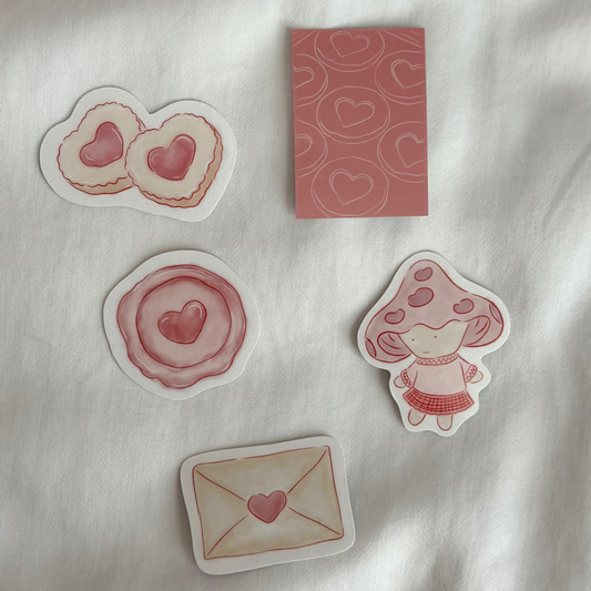 Five stickers displayed up close on a white background, featuring a pair of cookies, mini art print, stamp seal, a mushroom character, and an envelope.
