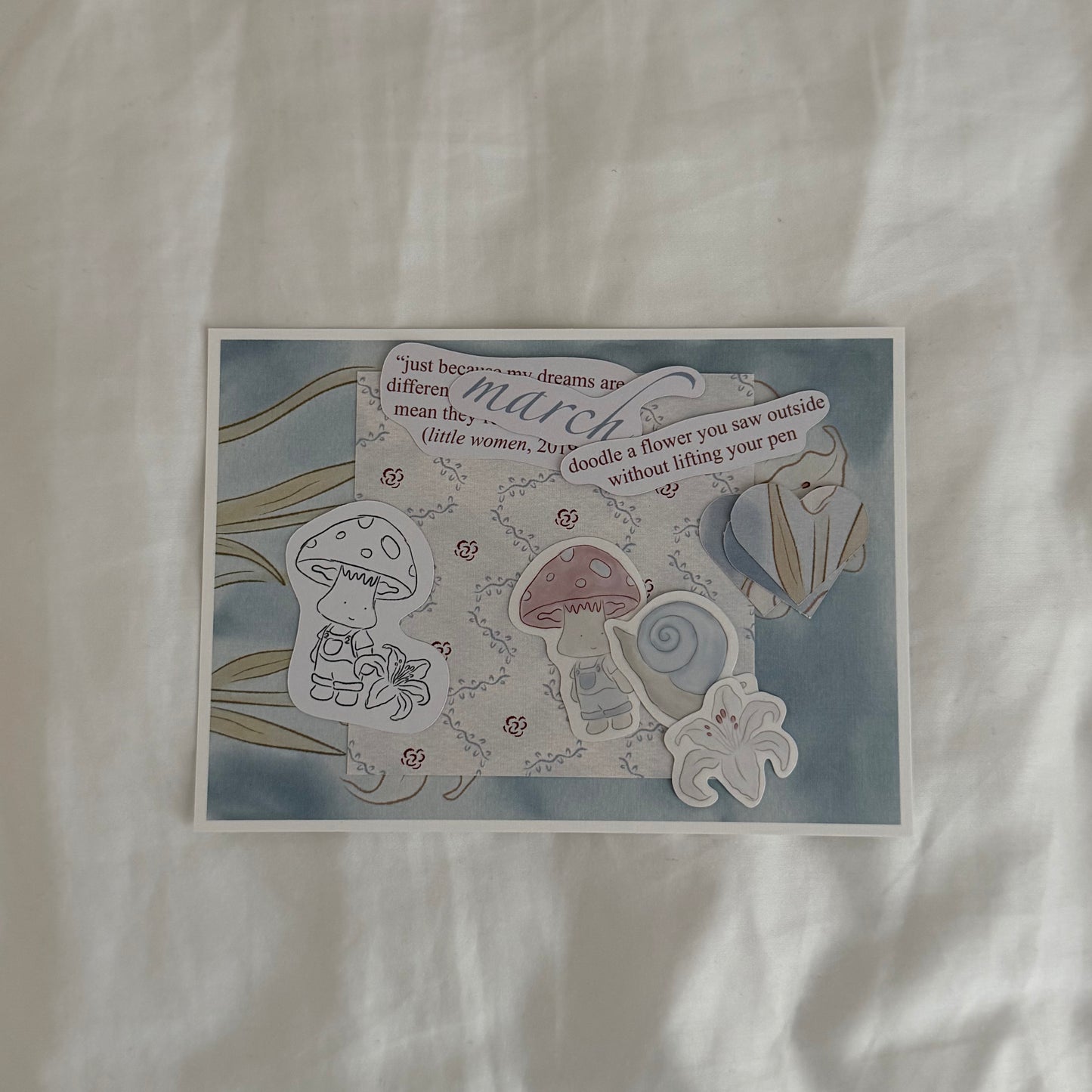 Inside an open envelope: 5x7 white lily print, 4x4 matching patterned print in soft blues, three matte stickers, journal and activity prompts, a mini mushroom coloring card, mini journaling cards, and three small lined paper hearts.