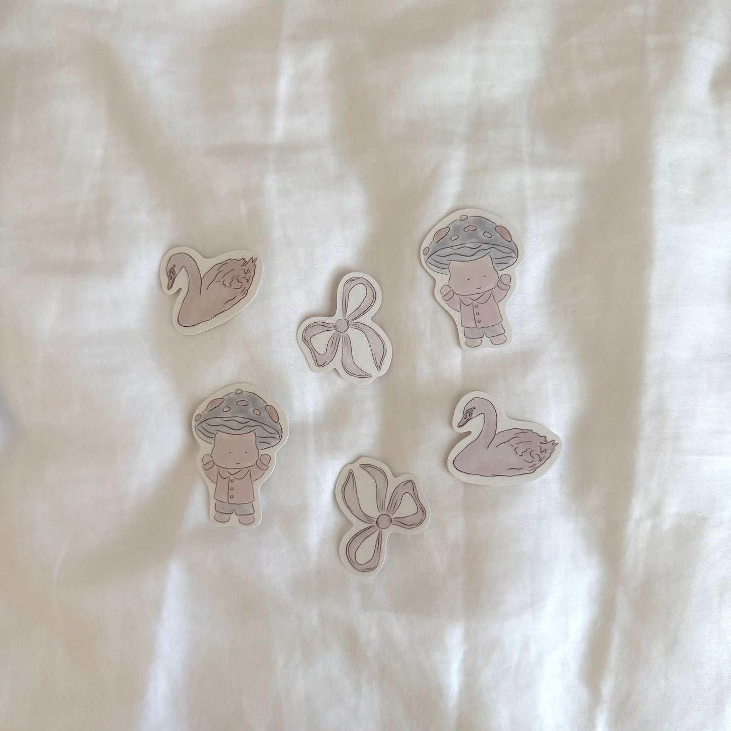 Six stickers displayed up close on a white background, featuring two swans, two mushroom characters, and two bows (each design repeated twice).