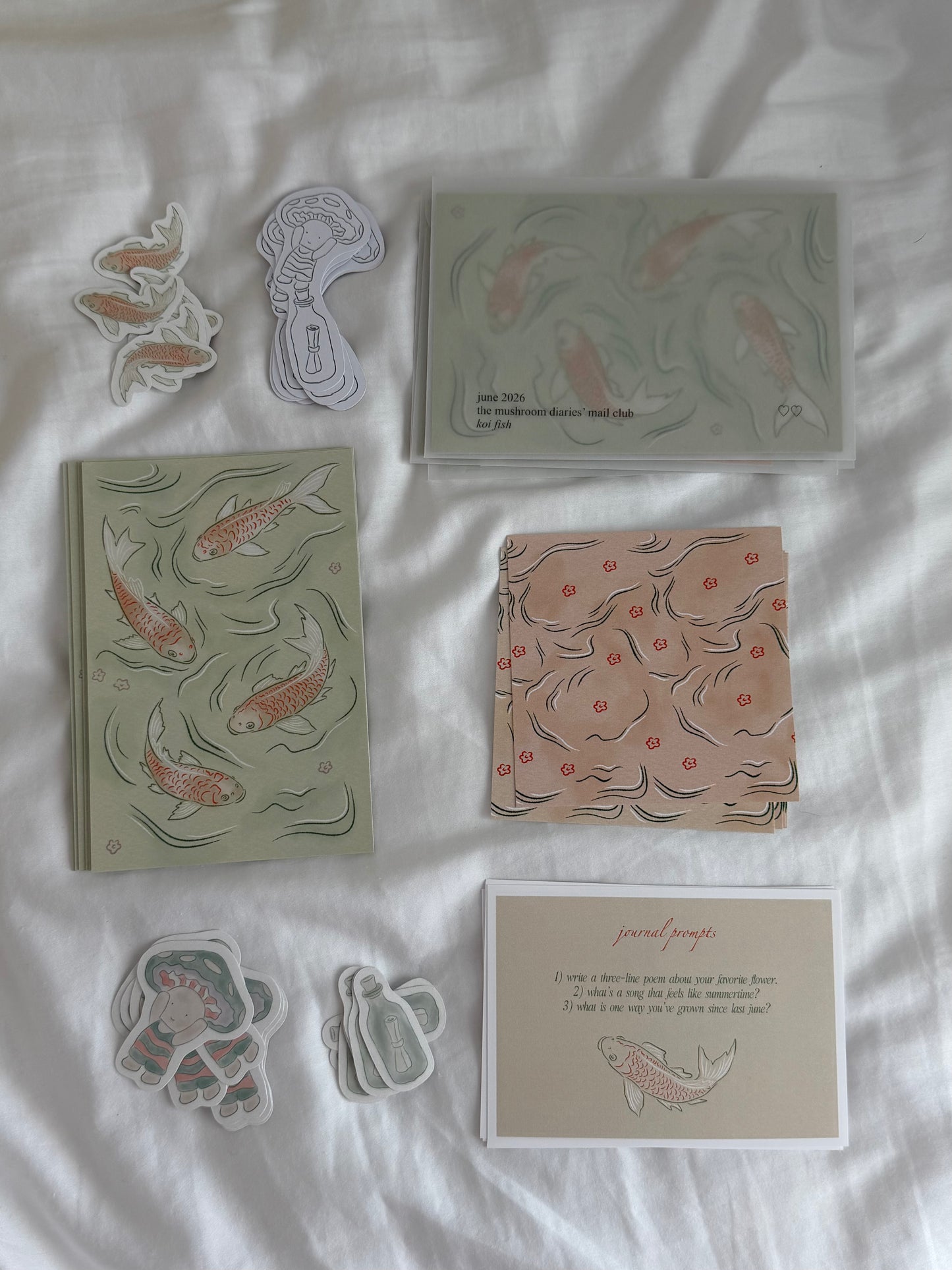 Collection of stationery items including notebooks, cards, and stickers with koi fish designs on a white fabric background.