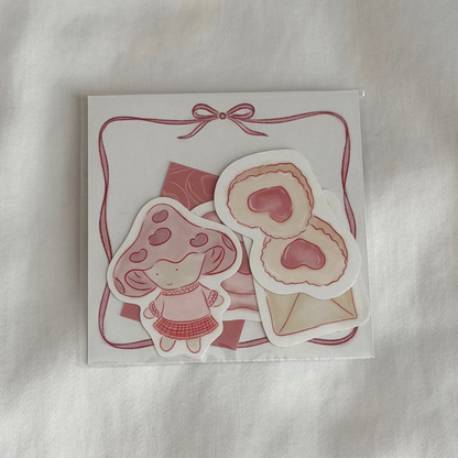 Five-piece sticker set with illustrated designs of a pair of cookies, mushroom character, mini art print, an envelope and a stamp seal, plus a 3x3 memo paper sheet, packaged in a clear sleeve on a white background.