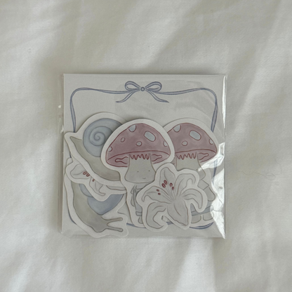 Six-piece sticker set with illustrated designs of a snail, mushroom character, and lily (two of each), plus a 3x3 memo paper sheet, packaged in a clear sleeve on a white background.
