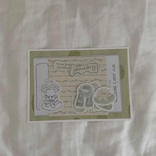 Inside an open envelope: 5x7 water lily print, 4x4 matching patterned print in soft sage green tones, five matte stickers, journal and activity prompts, a mini mushroom coloring card