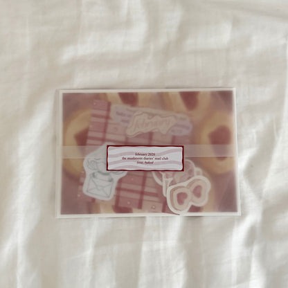 Envelope containing a 5x7 cookie art print, a 4x4 matching dainty patterned art print in red tones, five matte vinyl stickers, journal prompts, an activity prompt, a mini coloring card of a mushroom character (marker bleed-safe), mini cards for journaling