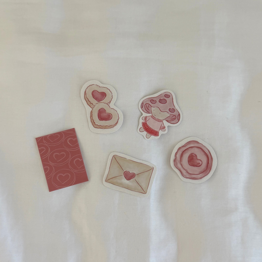 Five stickers displayed up close on a white background, featuring a pair of cookies, mini art print, stamp seal, a mushroom character, and an envelope.